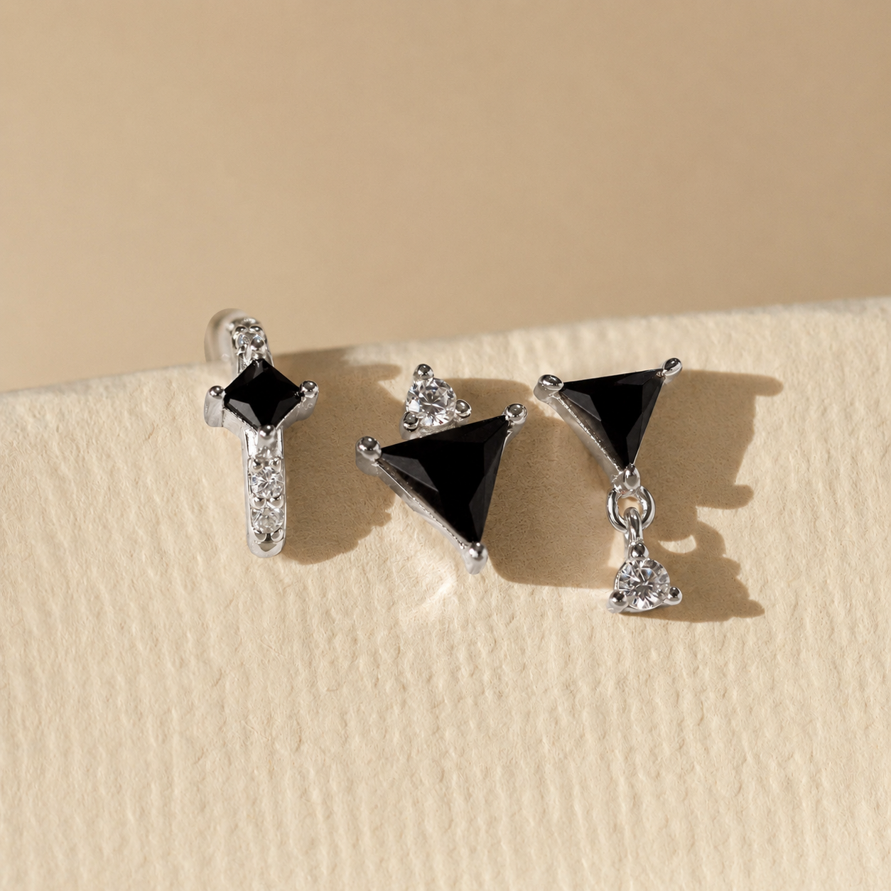 Pair of black triangle earrings with silver accents on a beige background