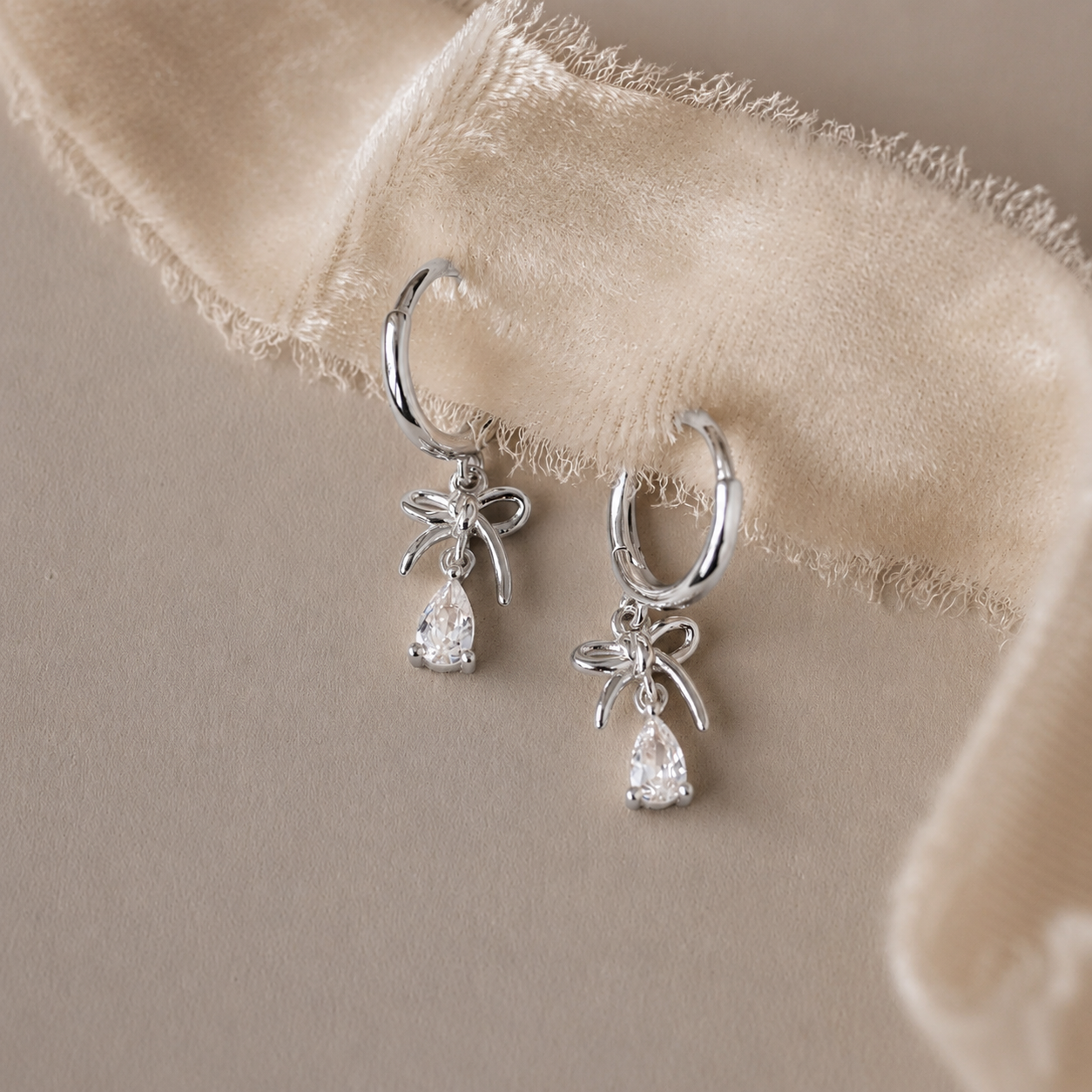 Silver hoop earrings with teardrop-shaped gemstones on a beige fabric background