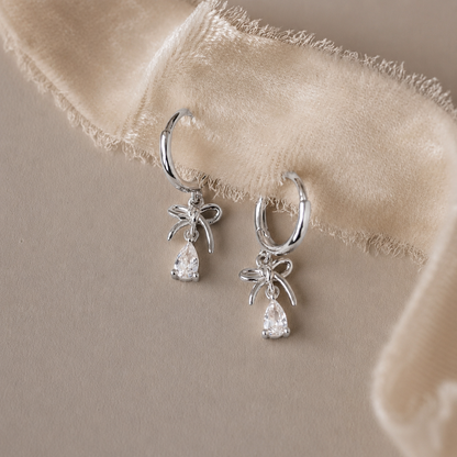 Silver hoop earrings with teardrop-shaped gemstones on a beige fabric background