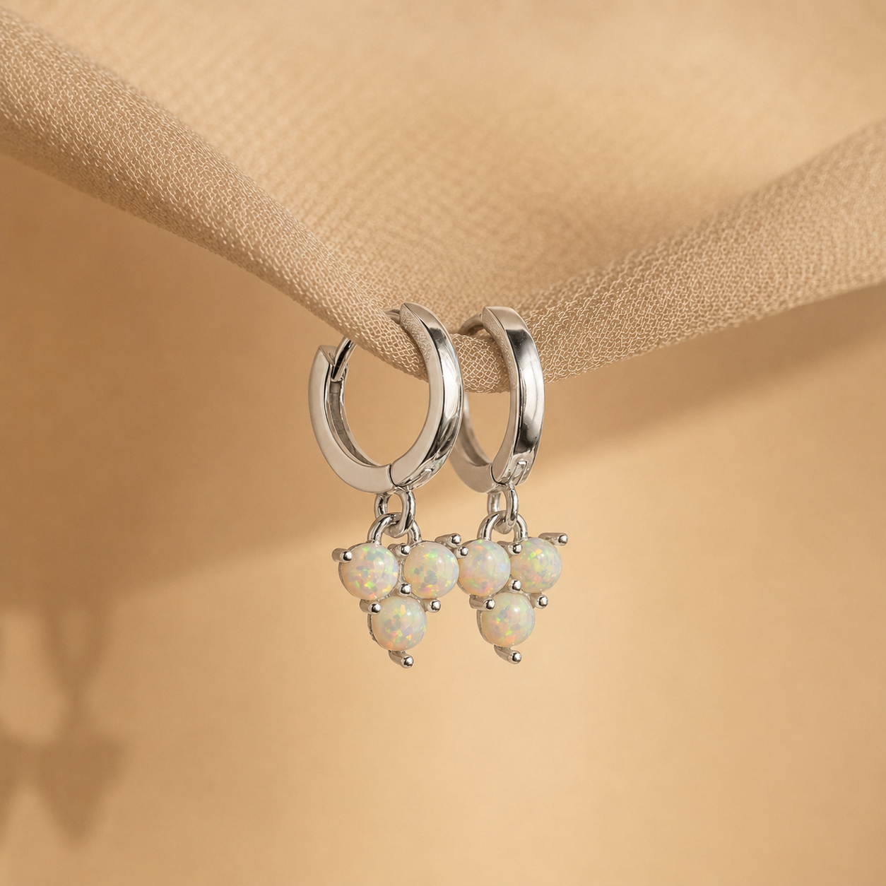 Silver hoop earrings with opal stones on a beige fabric background