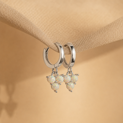Silver hoop earrings with opal stones on a beige fabric background