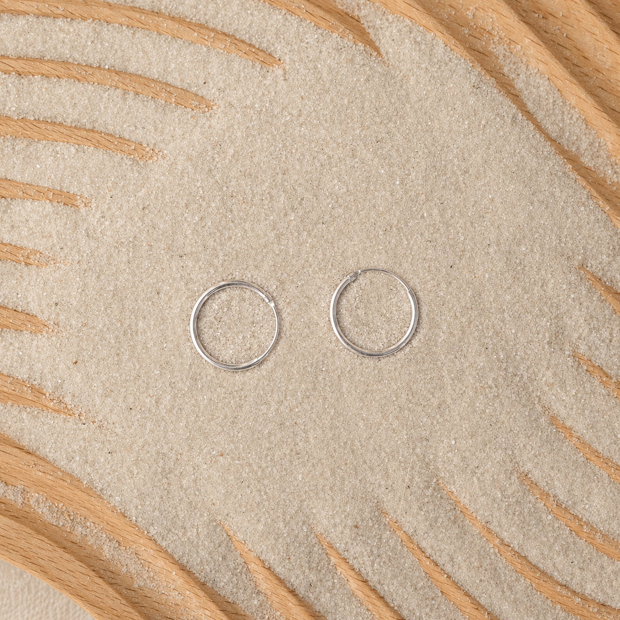 Two small silver circular jump rings placed on a textured beige surface with decorative wood rays.