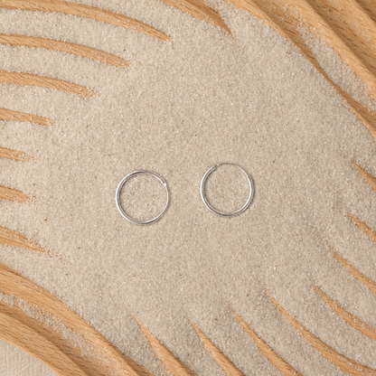 Two small silver circular jump rings placed on a textured beige surface with decorative wood rays.