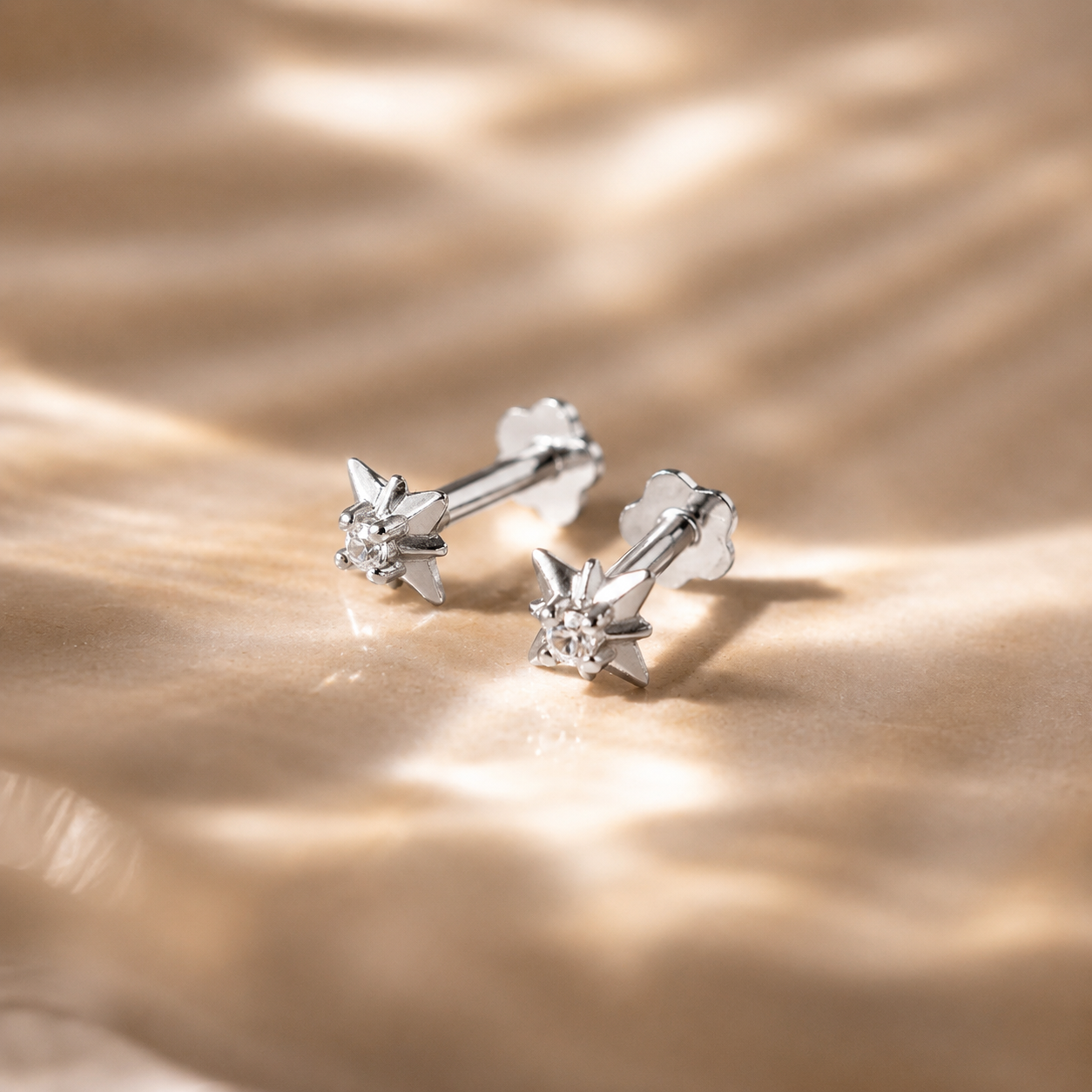 Pair of silver stud earrings on a textured beige surface