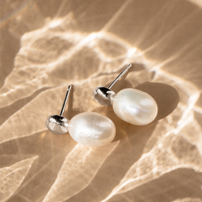 Pearl earrings on a textured beige surface with sunlight casting shadows