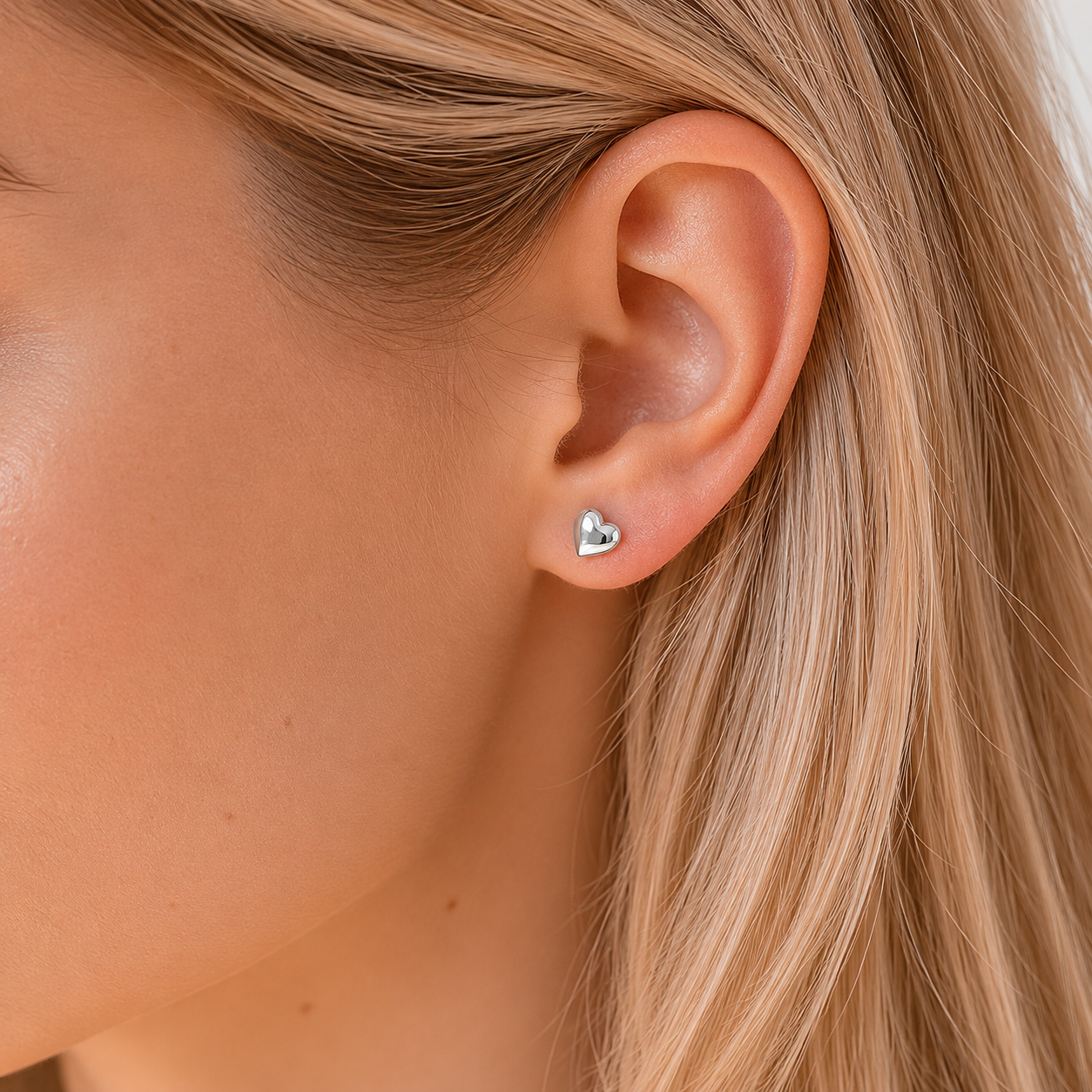 Close-up of an ear wearing a heart-shaped earring with blonde hair.