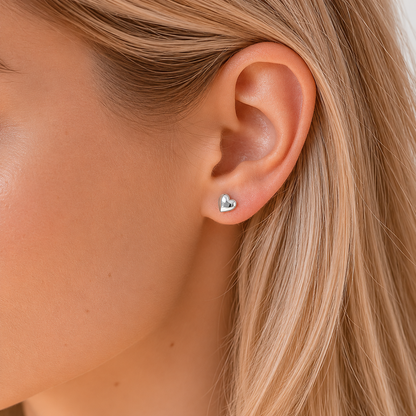 Close-up of an ear wearing a heart-shaped earring with blonde hair.