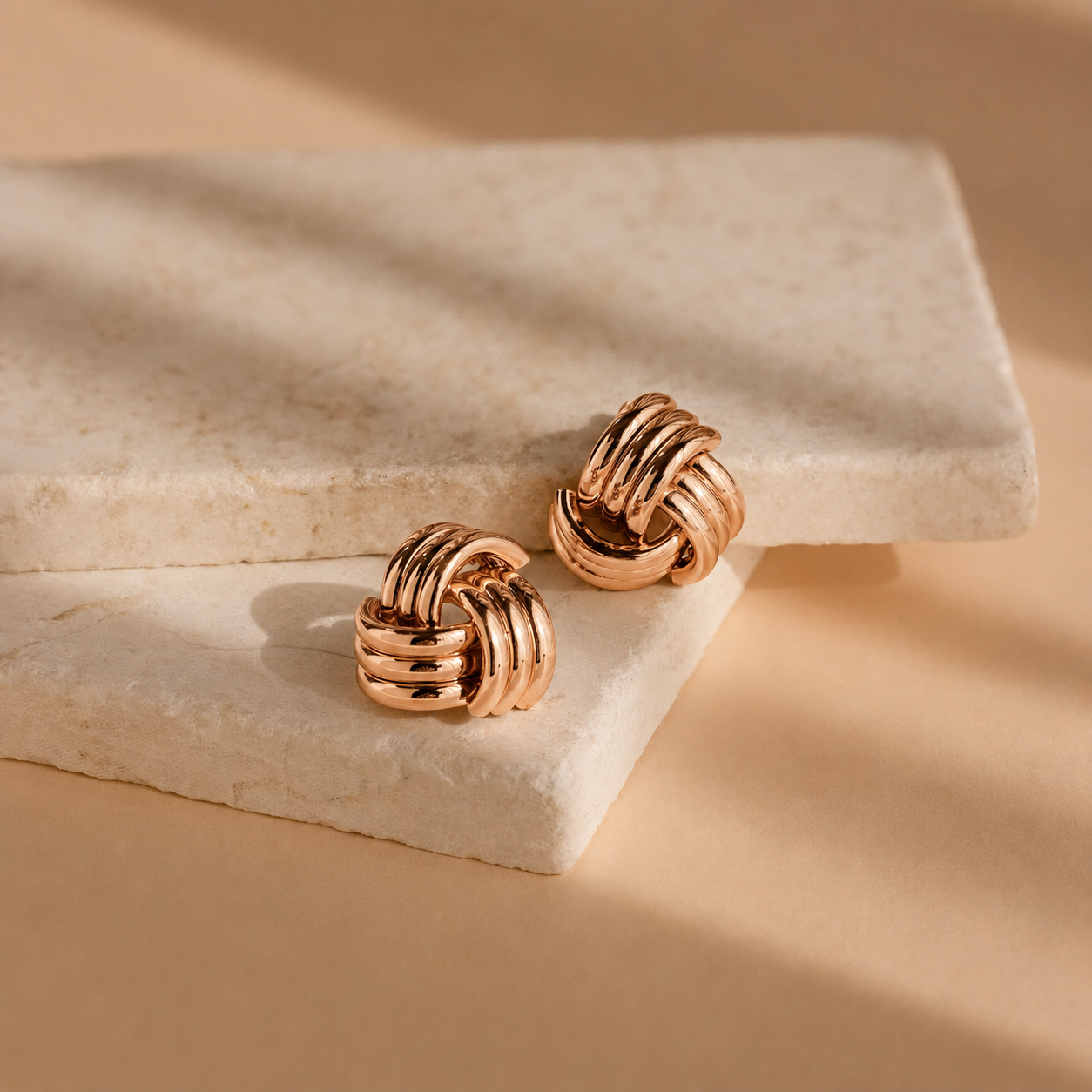 Pair of gold knot earrings on a beige stone surface