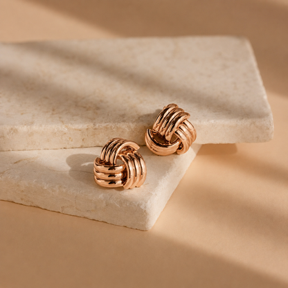 Pair of gold knot earrings on a beige stone surface