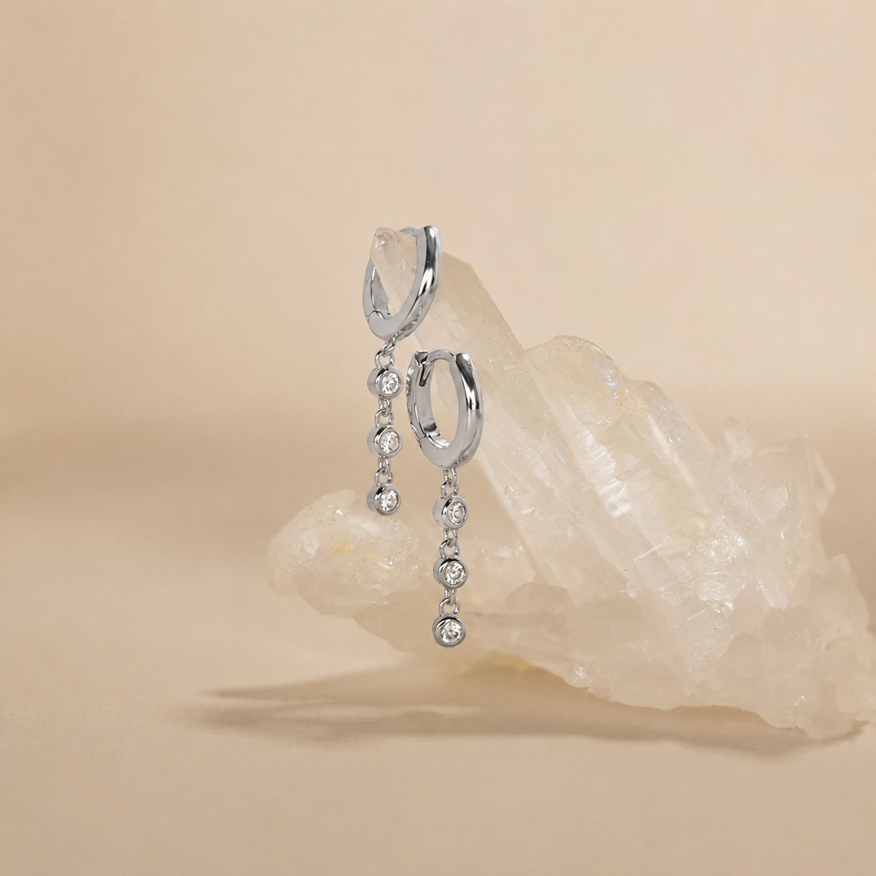 Silver earrings with dangling crystals on a beige background