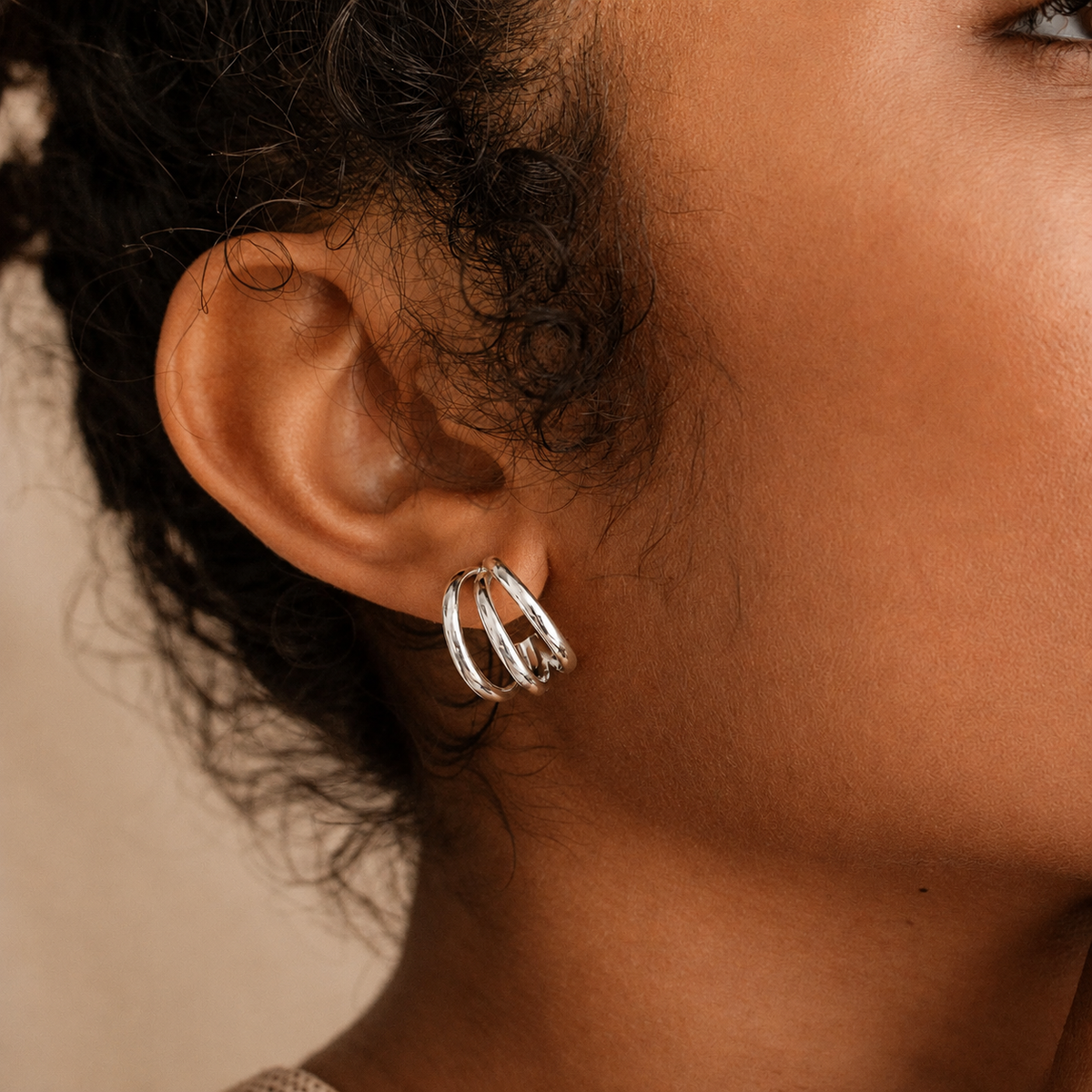 A close-up of a person's ear wearing a small silver hoop earring with three overlapping curved bands.