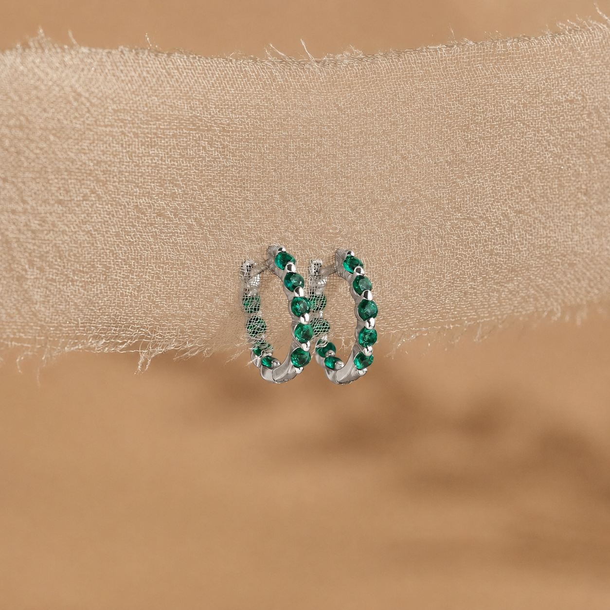 Pair of hoop earrings with green gemstones on a beige fabric background