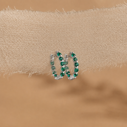 Pair of hoop earrings with green gemstones on a beige fabric background