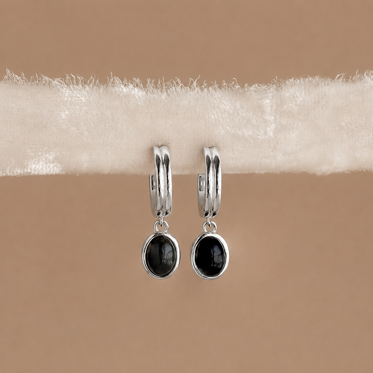 Silver hoop earrings with black gemstones on a beige background