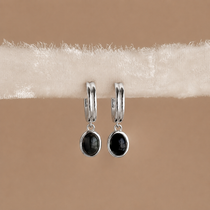 Silver hoop earrings with black gemstones on a beige background