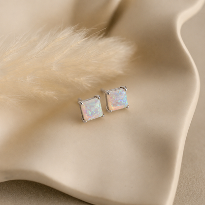 Square opal stud earrings on a beige fabric background