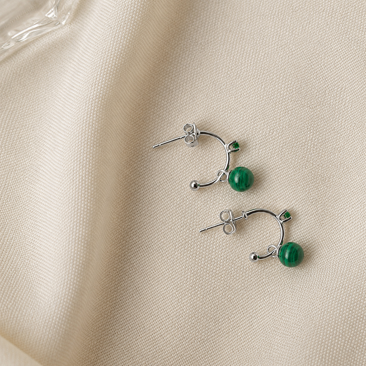 Pair of silver earrings with green beads on a beige fabric background