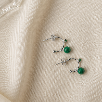 Pair of silver earrings with green beads on a beige fabric background