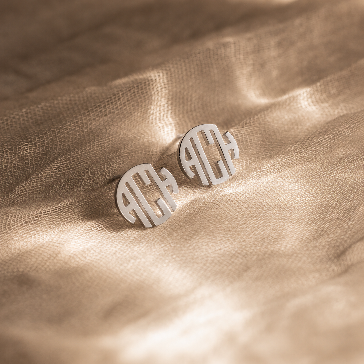 Silver monogram earrings on a beige fabric background