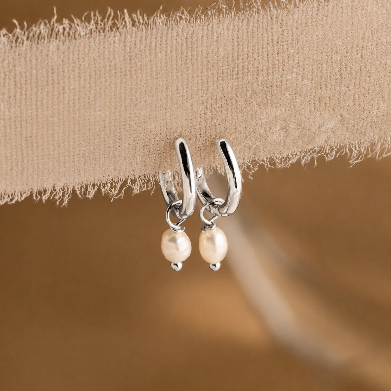 Silver hoop earrings with pearl drops on a beige fabric background