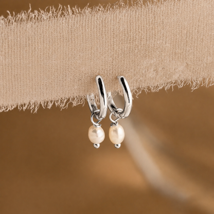 Silver hoop earrings with pearl drops on a beige fabric background