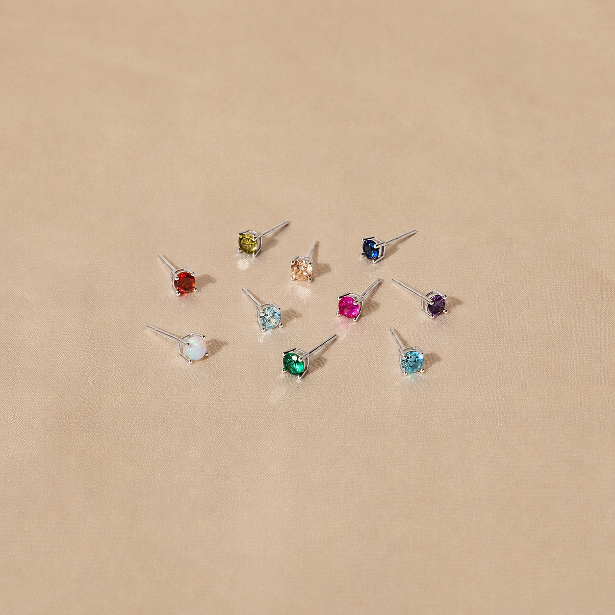 Set of small stud earrings with multicolored gemstones on a beige background
