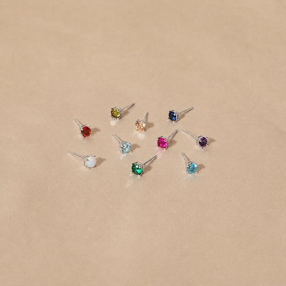 Set of small stud earrings with multicolored gemstones on a beige background