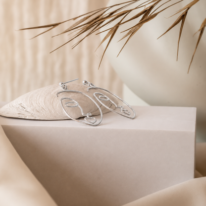 Silver hoop earrings on a beige surface with a soft background