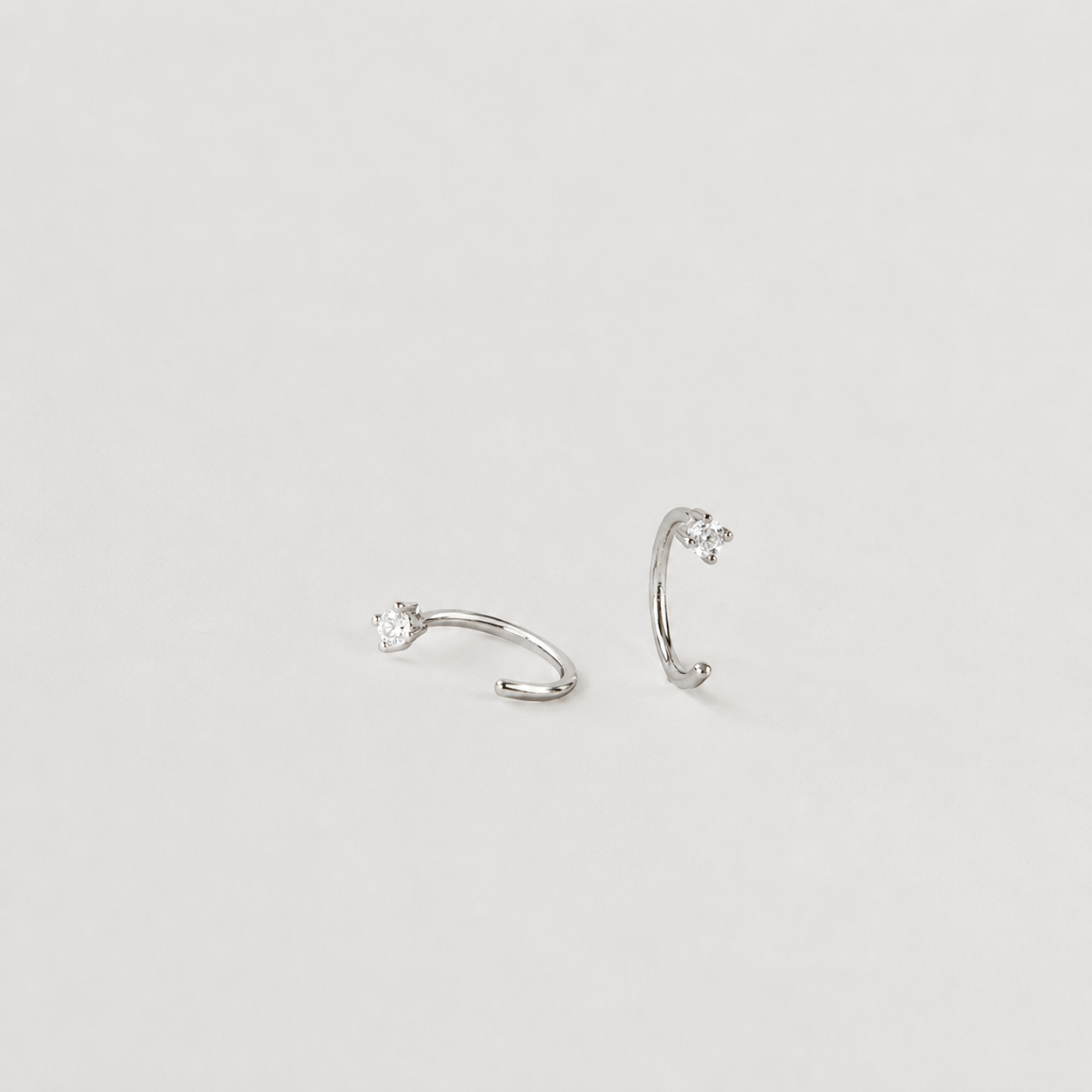 Pair of silver ear cuffs with small gemstones on a light gray background