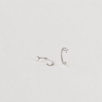 Pair of silver ear cuffs with small gemstones on a light gray background