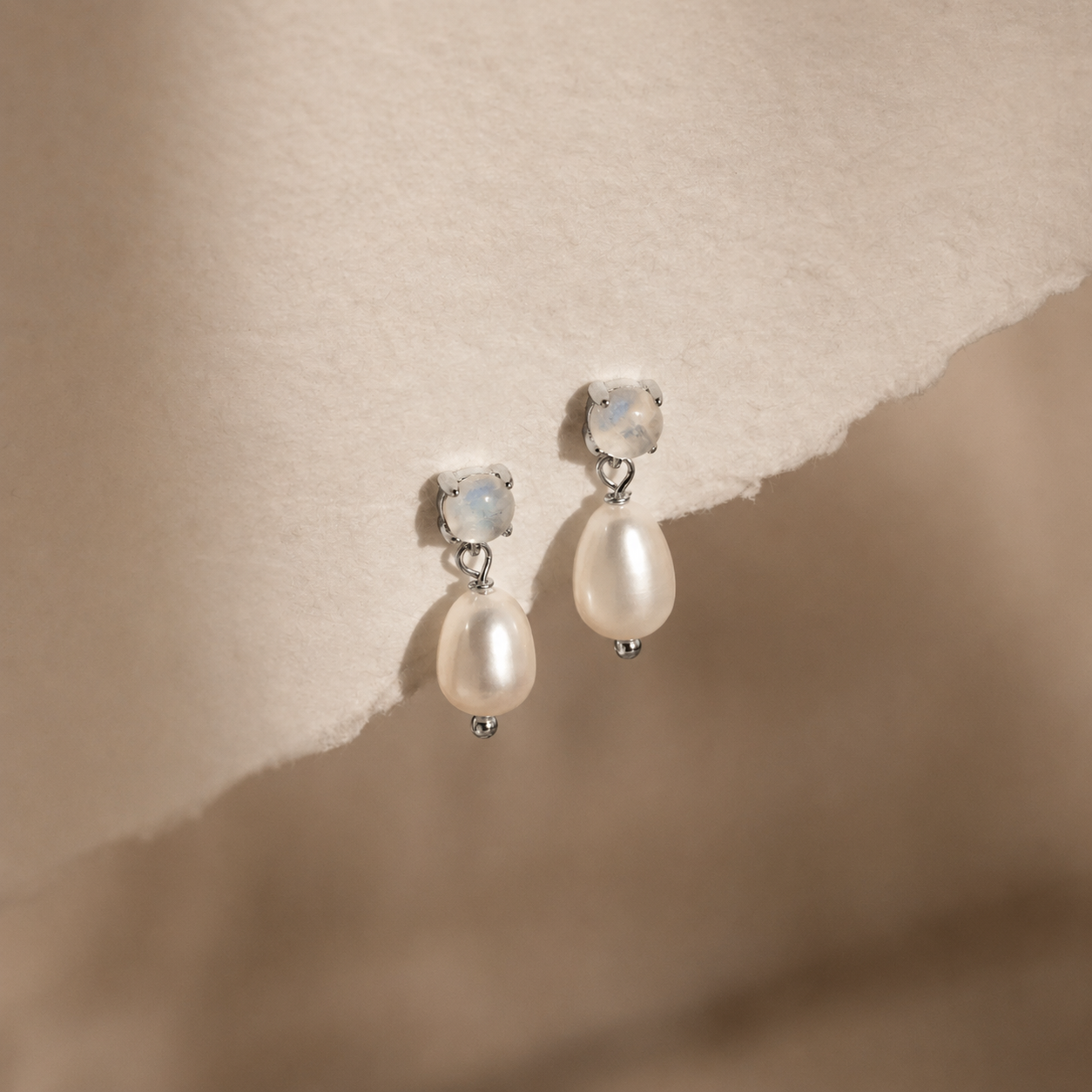 Pearl earrings with silver hooks on a textured beige background