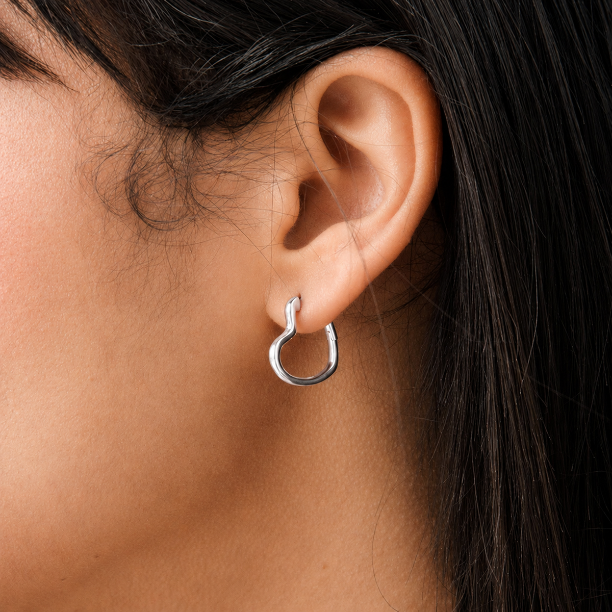Close-up of an ear wearing a gold hoop earring with dark hair partially visible.