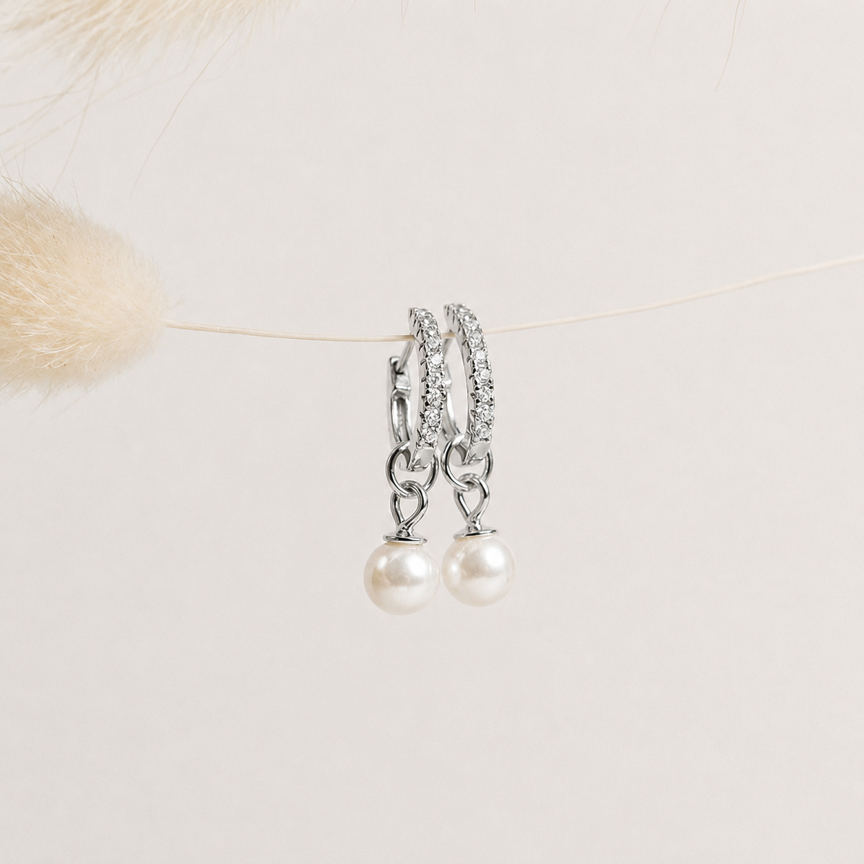 Pair of pearl earrings with silver chains on a light background