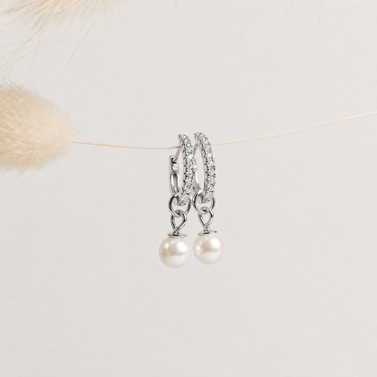Pair of pearl earrings with silver chains on a light background