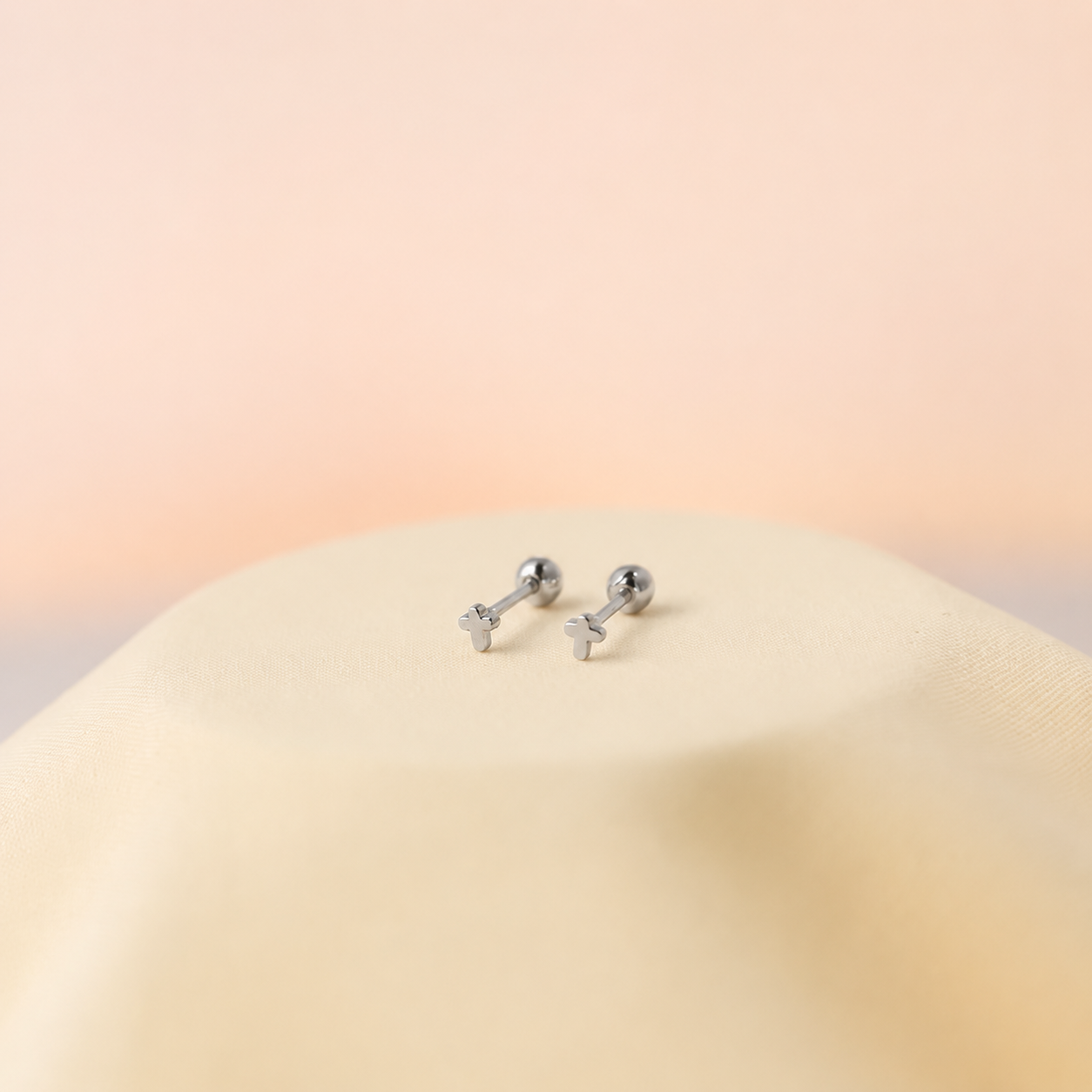 Pair of silver earrings on a beige surface with a soft pink background