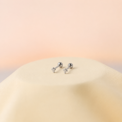 Pair of silver earrings on a beige surface with a soft pink background