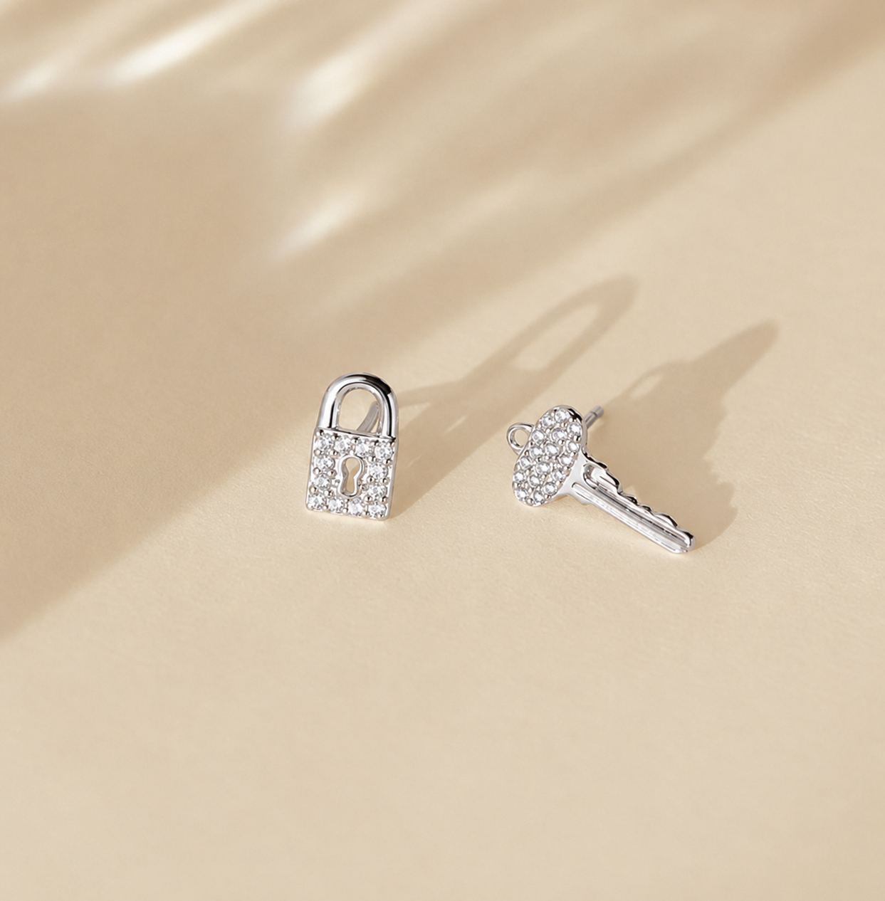 Silver padlock and key earrings on a beige background
