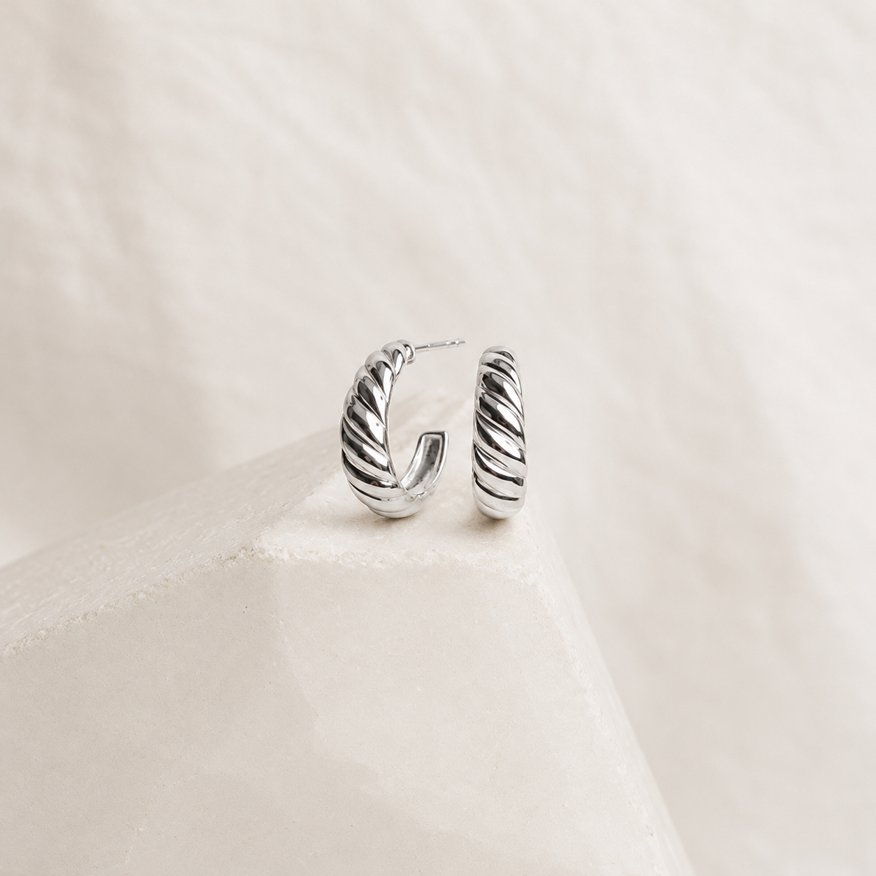 Silver hoop earrings on a light beige fabric background