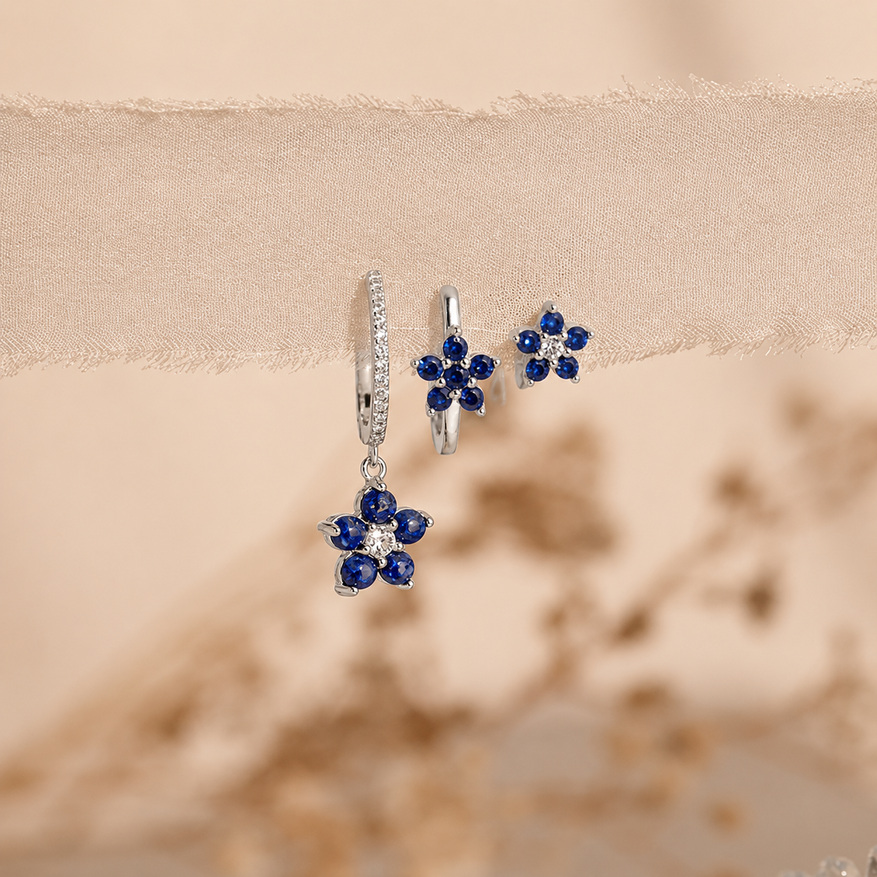 Flower-shaped earrings with blue gemstones on a beige fabric background
