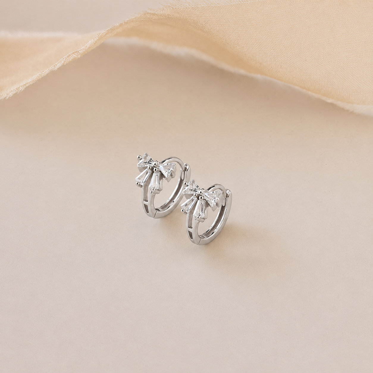 Silver hoop earrings on a beige fabric background