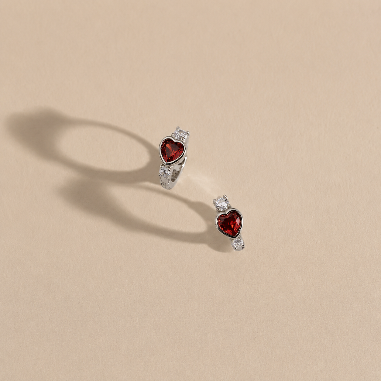 Heart-shaped red gemstone earrings on a beige background