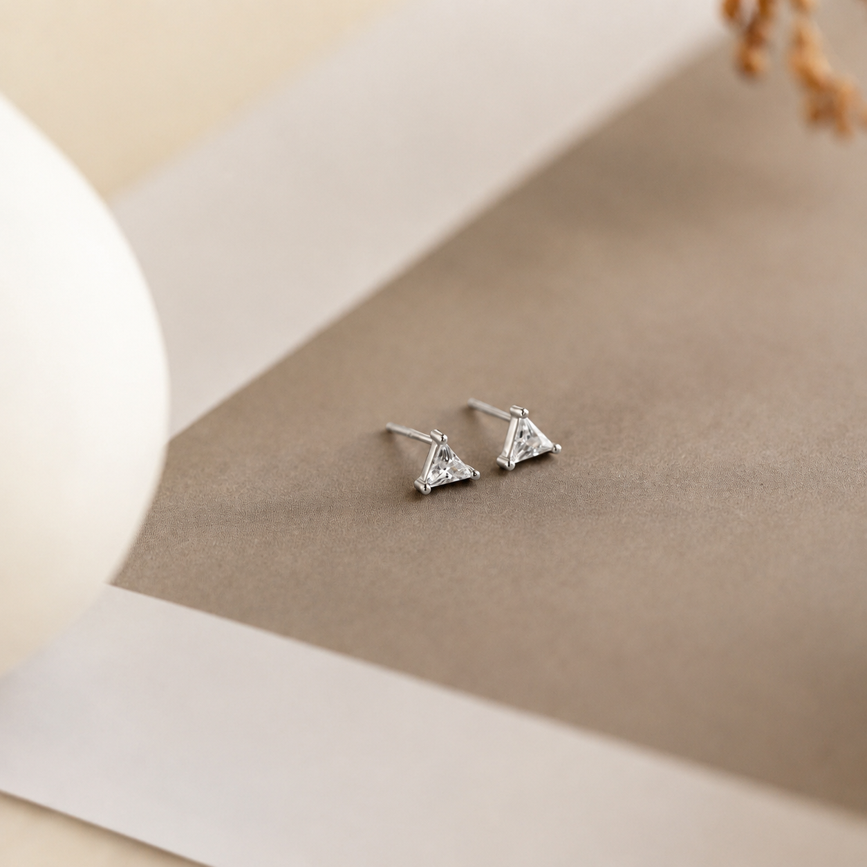 Pair of triangle-shaped stud earrings on a beige background