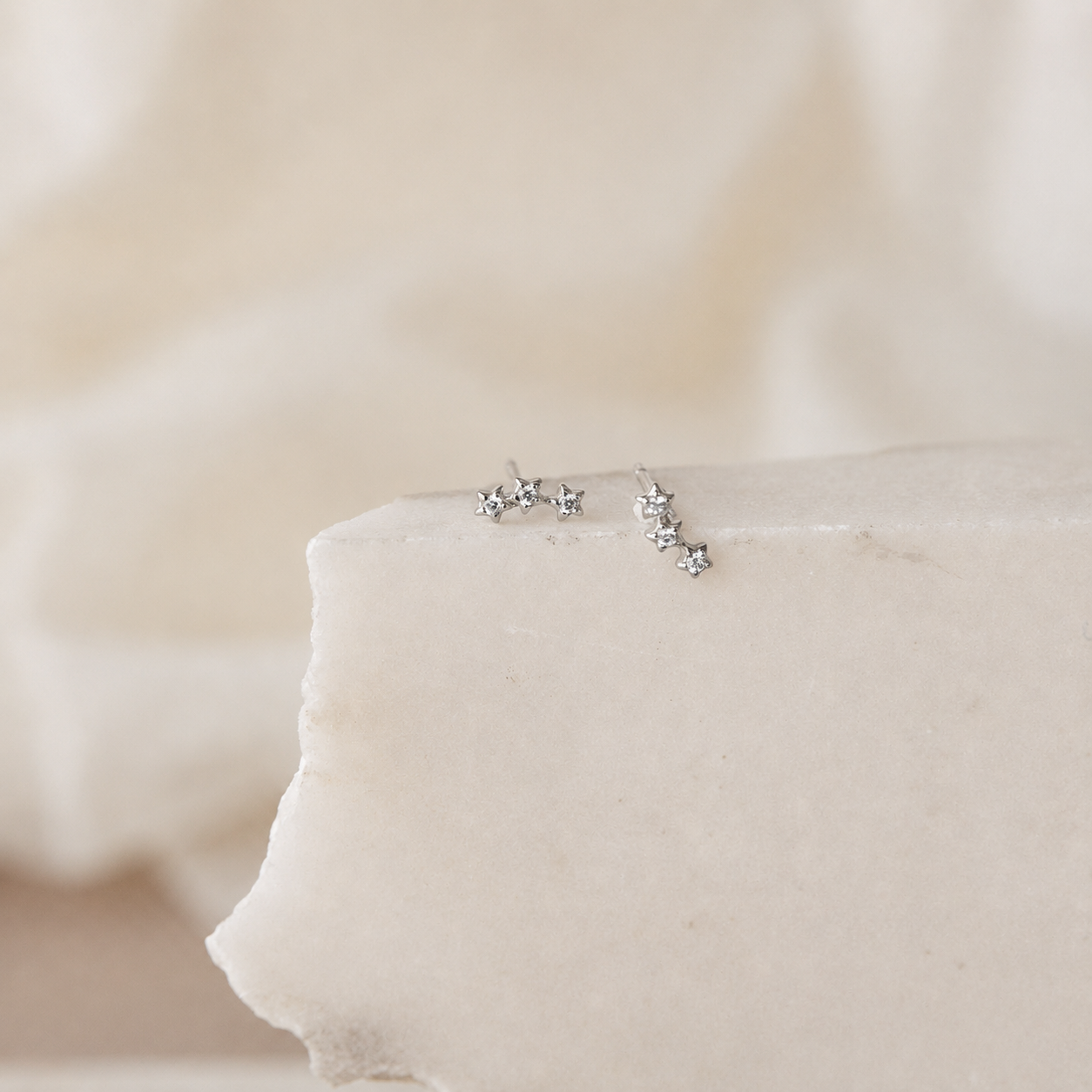 Silver star-shaped earrings on a soft beige fabric background