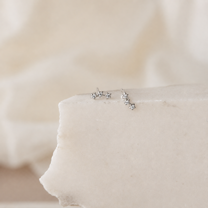 Silver star-shaped earrings on a soft beige fabric background