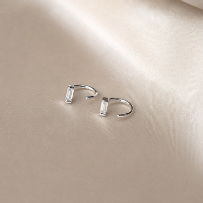 Pair of silver hoop earrings on a beige surface
