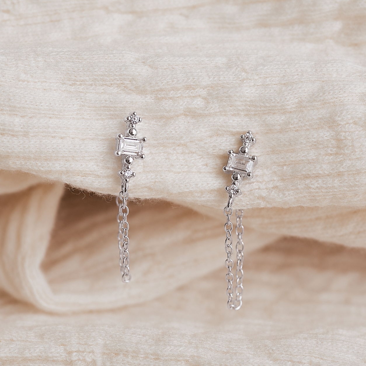 Pair of silver earrings with chain drops on a textured beige fabric background