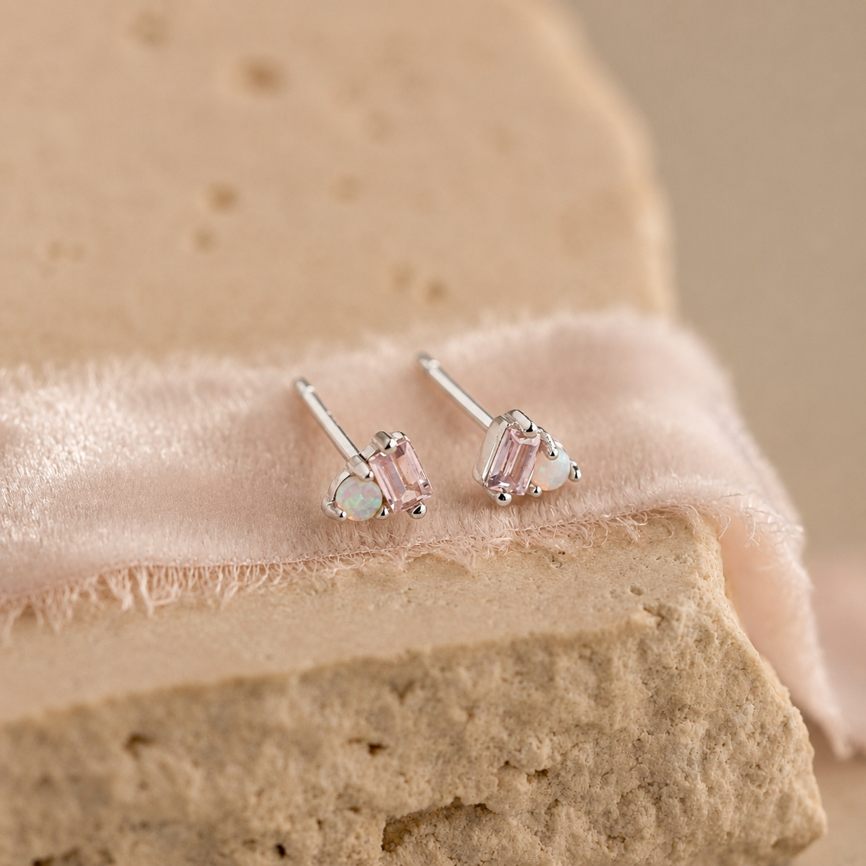Pair of silver earrings with pink gemstones on a beige fabric background