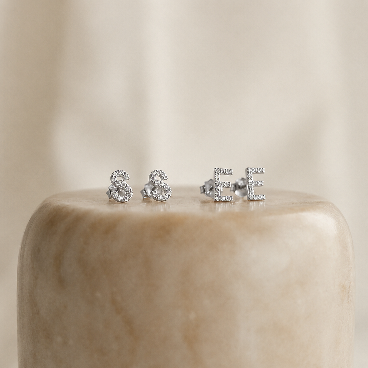 Three pairs of silver stud earrings on a beige marble surface with a neutral background