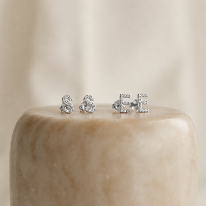 Three pairs of silver stud earrings on a beige marble surface with a neutral background