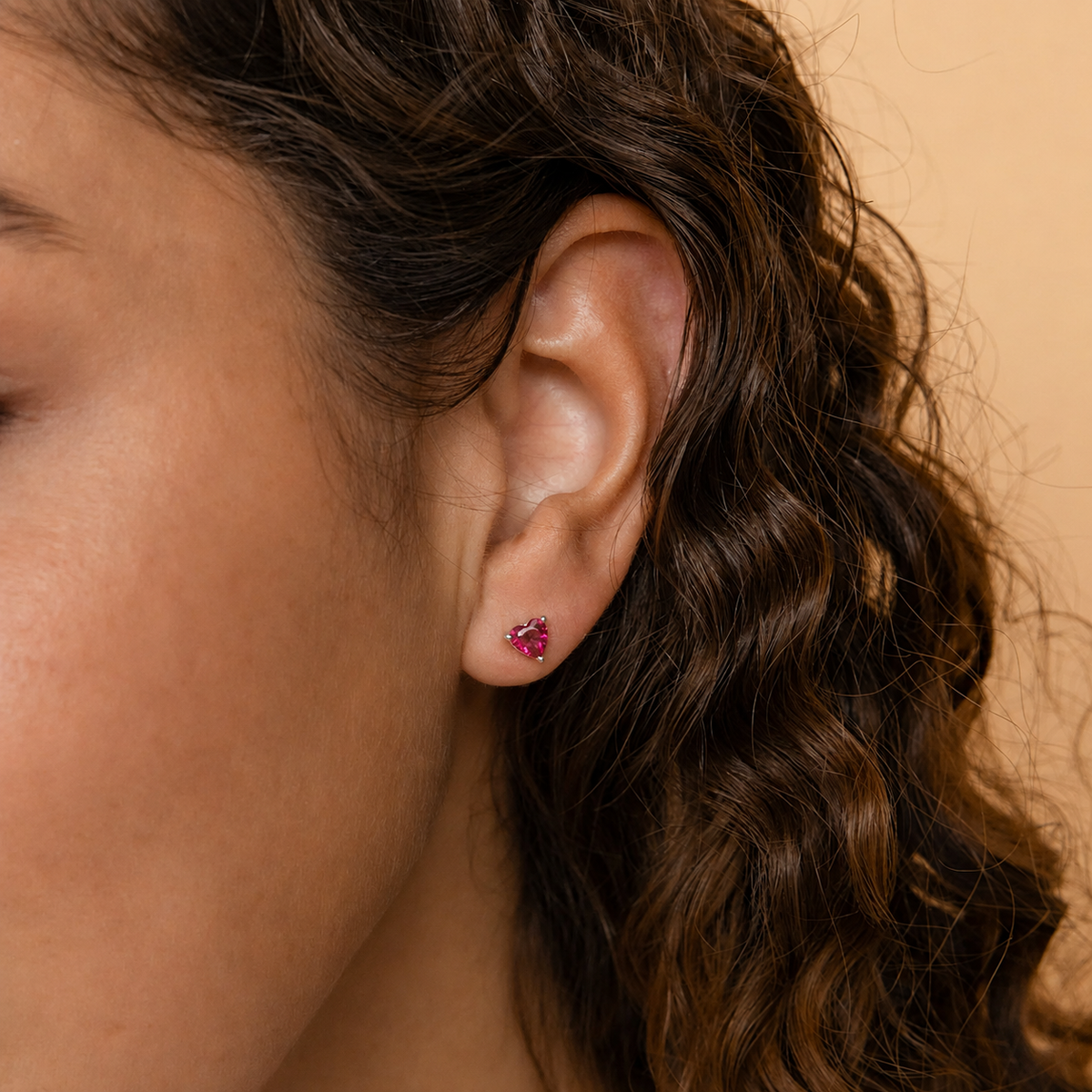 Close-up of an ear with a pink earring against a beige background